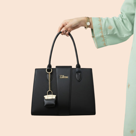 Black handbag with gold tag held by a hand against a beige background