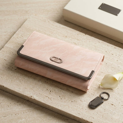 Pink wallet with black accents on a light wooden surface with a keychain and white flower.