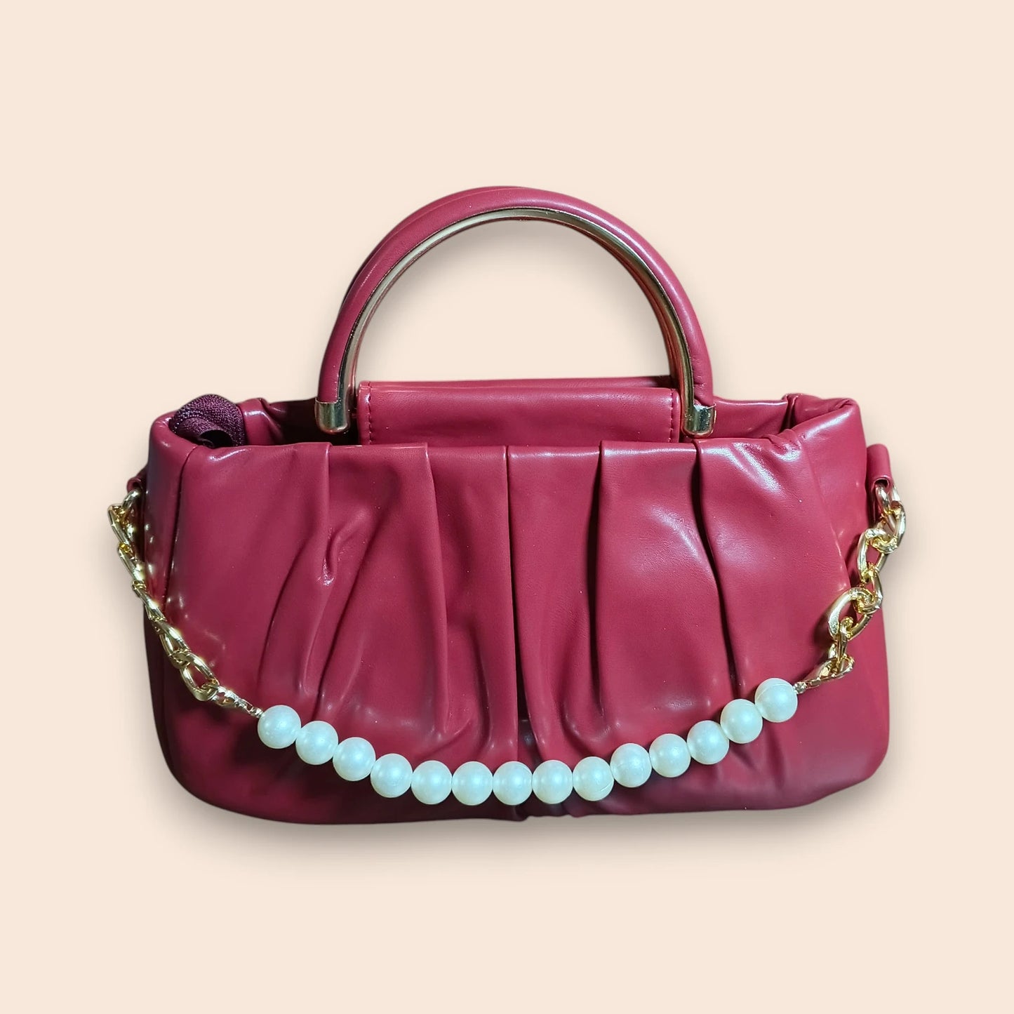 Maroon handbag with a gold chain and white beads on a beige background
