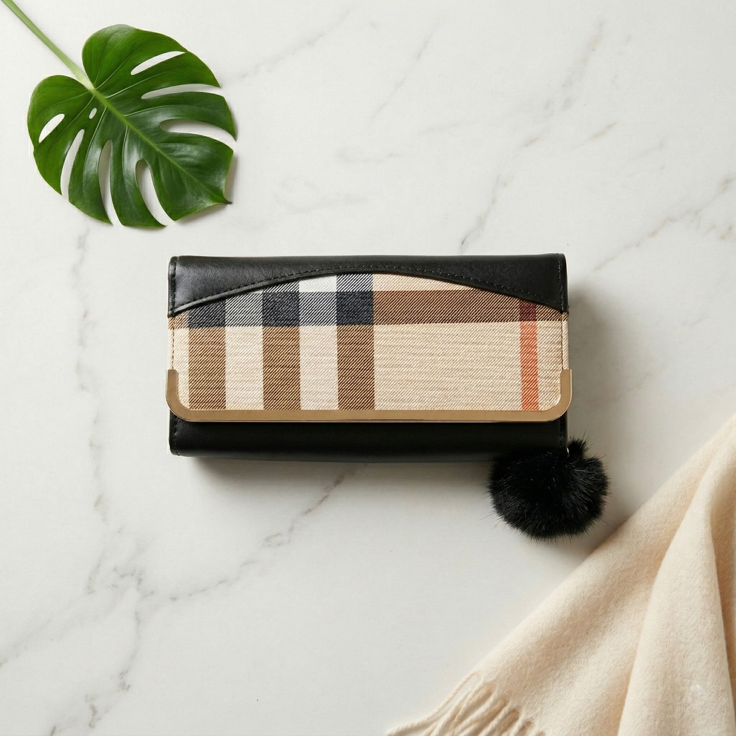 Wallet with plaid design on a marble surface with a leaf and fabric.