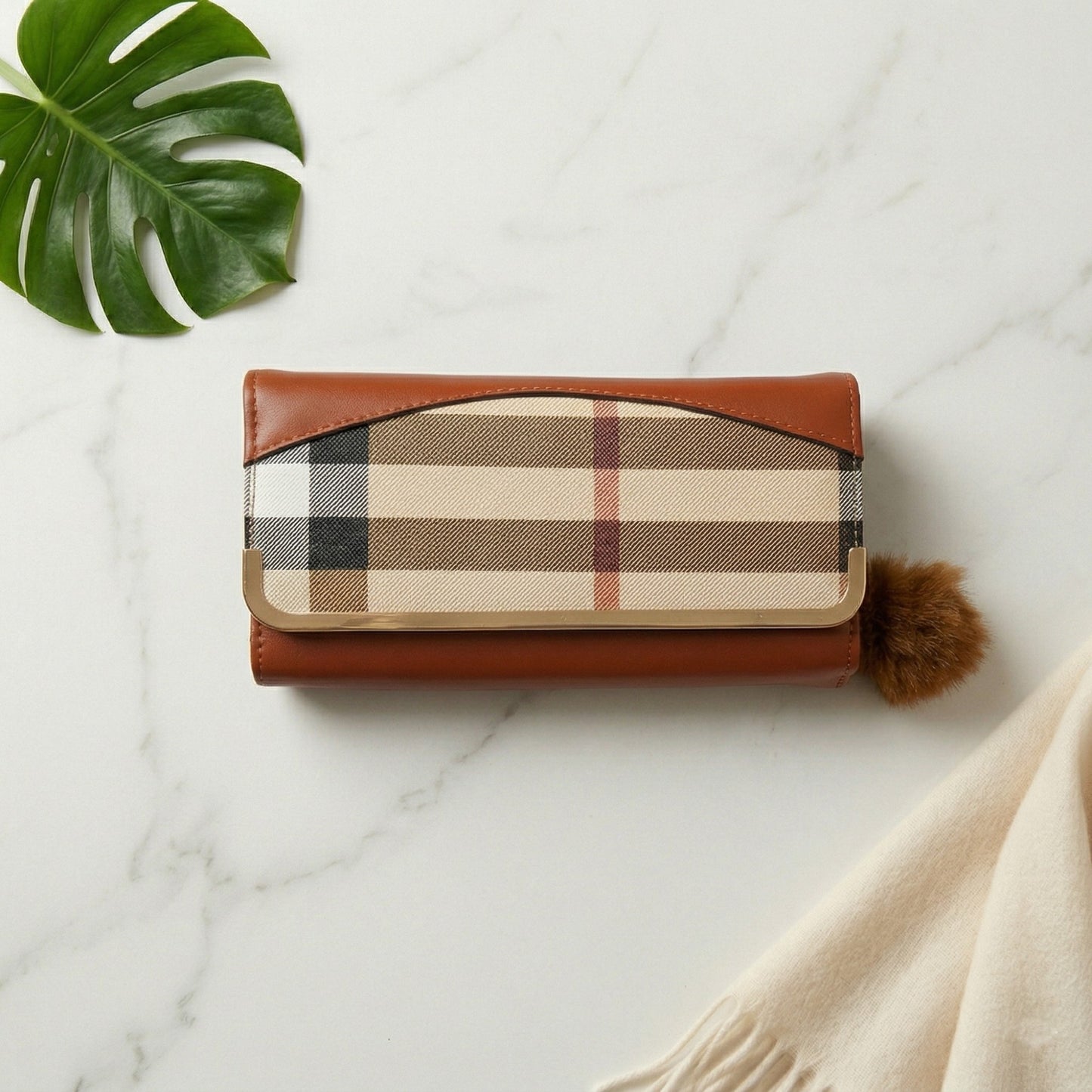 Plaid wallet with brown leather accents on a marble surface with a leaf and fabric item.